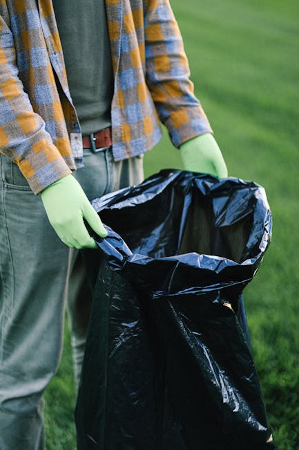 Two large black plastic bags filled with rubbish, tied at the top, are placed on the pavement beside a black metal fence and a brick wall. The bags appear to contain household waste or discarded items